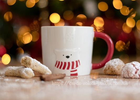 Weiße Eisbär-Tasse mit rotem Schal neben Puderzucker-Plätzchen und einem Zimtstab