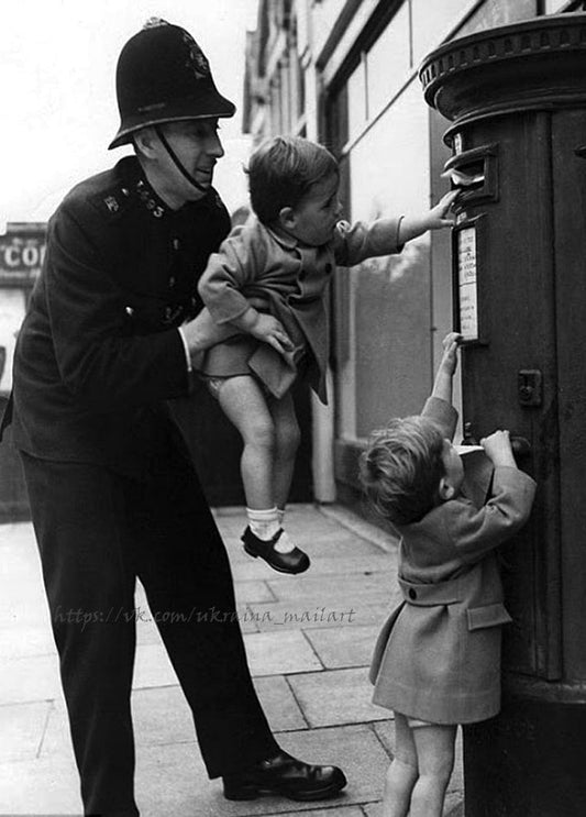 Polizist hebt ein Kleinkind zum Briefkasten, während ein zweites Kind einen Brief einwirft