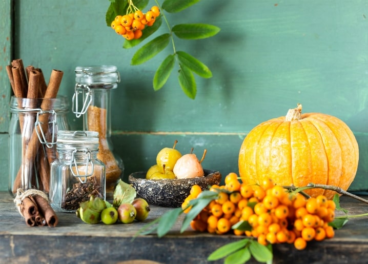 Pumpkin, cinnamon sticks, and orange rowan berries arranged in an autumn still life on a green table.