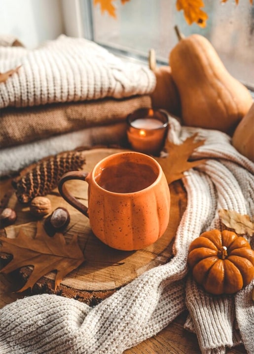 Pumpkin-shaped mug of cocoa among a knit sweater, candle and mini pumpkins