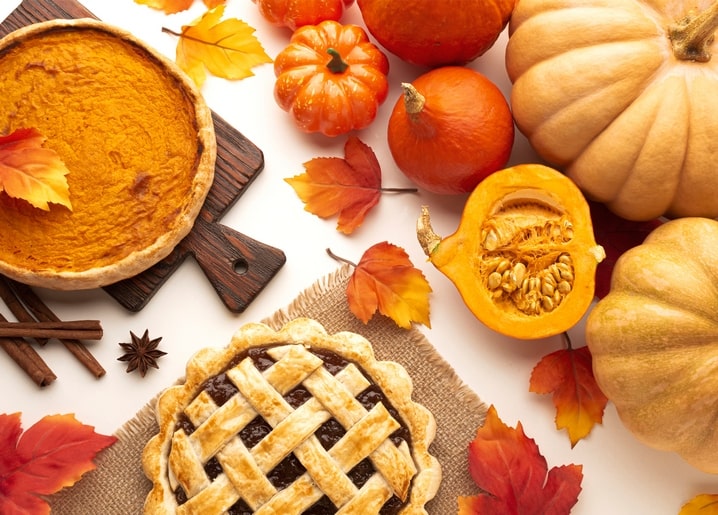 Pumpkin pie and lattice-crust pie surrounded by whole pumpkins, cinnamon sticks and autumn leaves