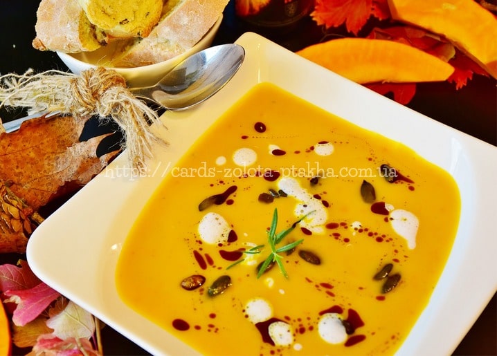 Bowl of pumpkin soup with cream swirls, seeds, and rosemary, served with toasted bread