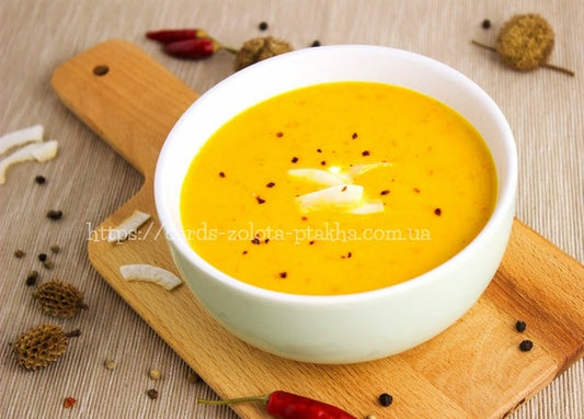 Bowl of creamy pumpkin soup with chili flakes and white shavings on a wooden board
