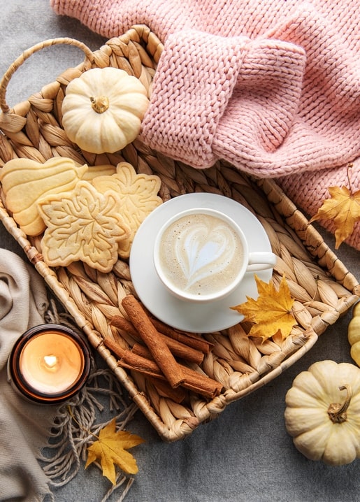 Geflochtenes Tablett mit Mini-Kürbissen, Ahornblatt-Keksen, Zimtstangen und Latte mit Herzmuster