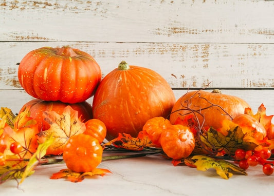 Orange pumpkins of various sizes with maple leaves and red berries on whitewashed wood planks