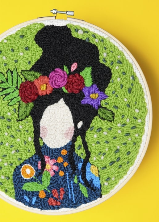 Punch-needle embroidery of a girl's silhouette crowned with roses and wildflowers in a green hoop