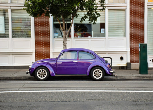 Klassischer lila Volkswagen Käfer parkt an einer backsteingesäumten Stadtstraße