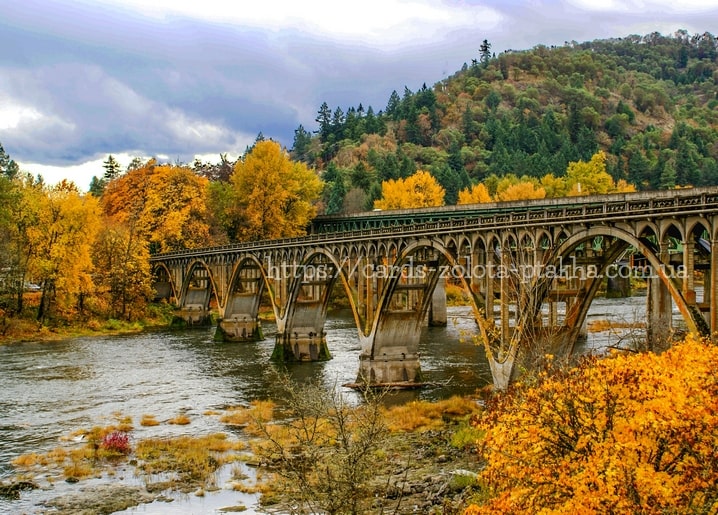 Concrete railway trestle bridge spanning a mountain river amid golden autumn trees