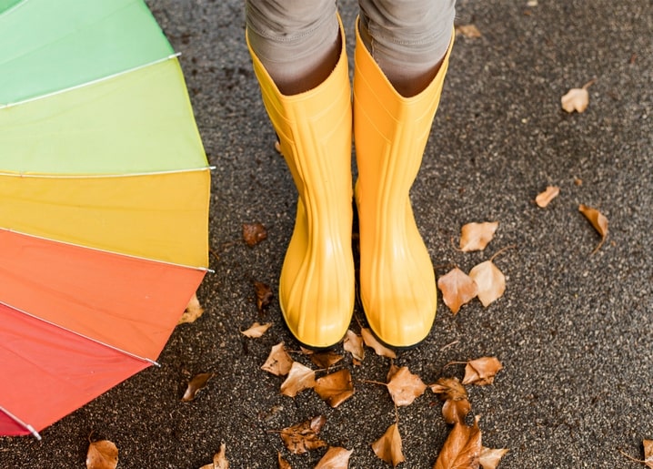 Yellow rain boots and open rainbow umbrella on fallen autumn leaves