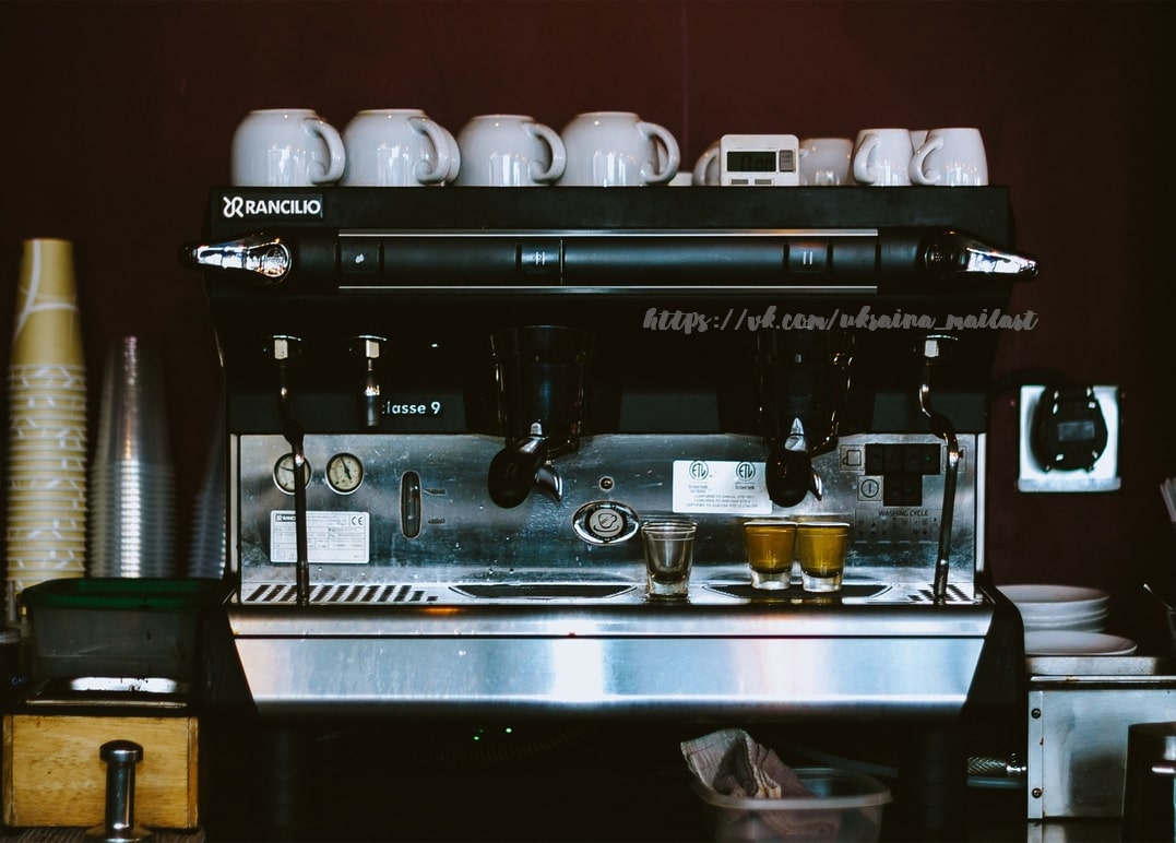 Rancilio-Espressomaschine zieht Espresso an einer dunklen Kaffeebar mit gestapelten Bechern
