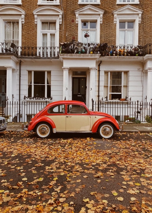 Vintage red Volkswagen Beetle parked on a London street covered in autumn leaves