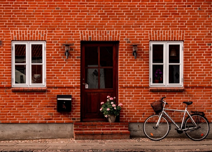 Red brick house facade with white windows and a bicycle parked by the door