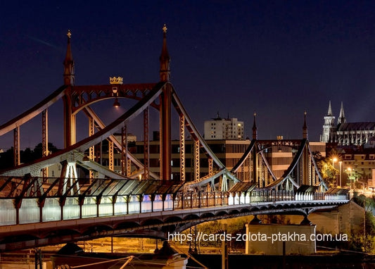 Rote Stahlbrücke mit kronengeschmückten Türmen leuchtet nachts vor der Skyline mit Kathedralenspitzen.