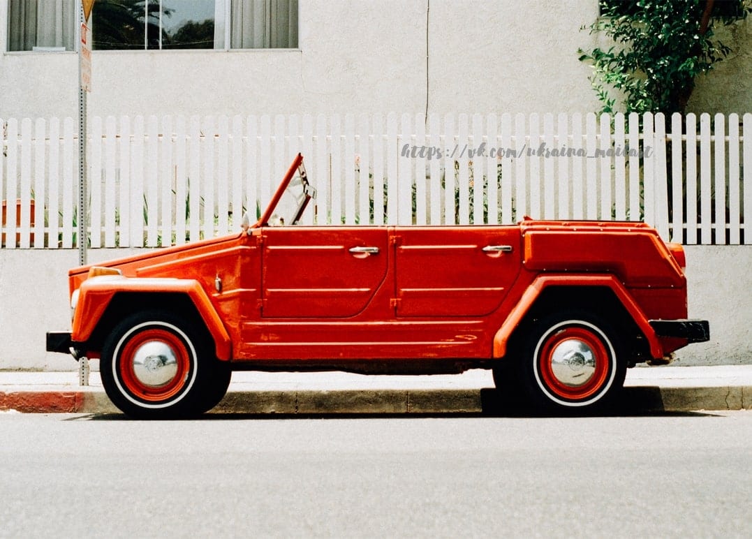 Rotes Oldtimer-Cabrio geparkt an einem weißen Lattenzaun
