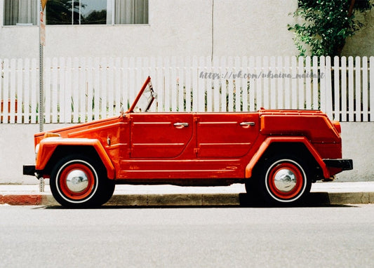Rotes Oldtimer-Cabrio geparkt an einem weißen Lattenzaun