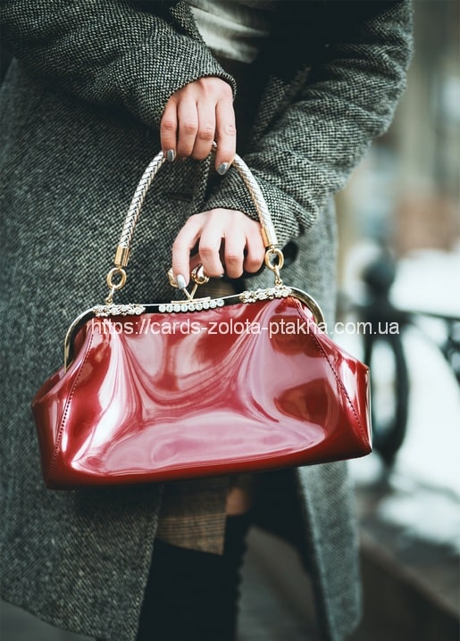Nahaufnahme einer roten Lacklederhandtasche mit Flechtgriff vor einem Tweedmantel
