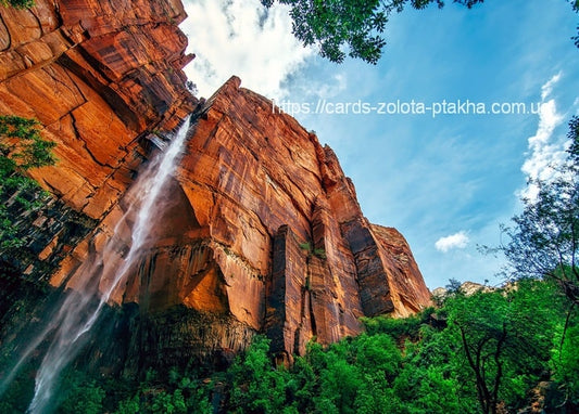 Wasserfall an einer roten Sandsteinwand im Canyon vor blauem Himmel