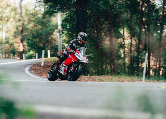 Rot-weißes Sportmotorrad neigt sich in einer Waldkurve
