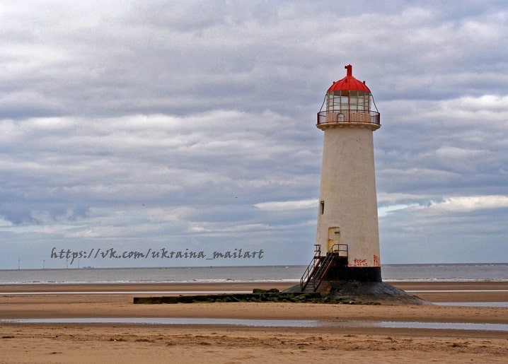Weißer Leuchtturm mit rotem Laternenaufsatz allein am Sandstrand bei Ebbe unter bewölktem Himmel