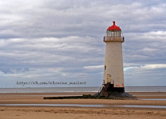 Weißer Leuchtturm mit rotem Laternenaufsatz allein am Sandstrand bei Ebbe unter bewölktem Himmel
