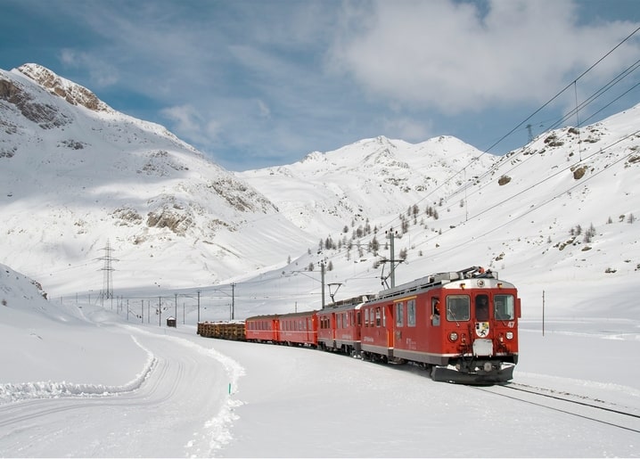 Roter Zug fährt durch ein schneebedecktes Alpental