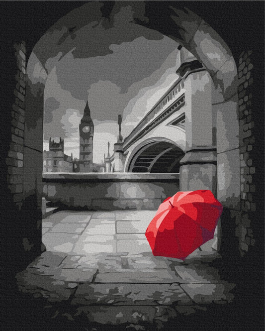 Black-and-white archway view of Big Ben with a single red umbrella on the ground