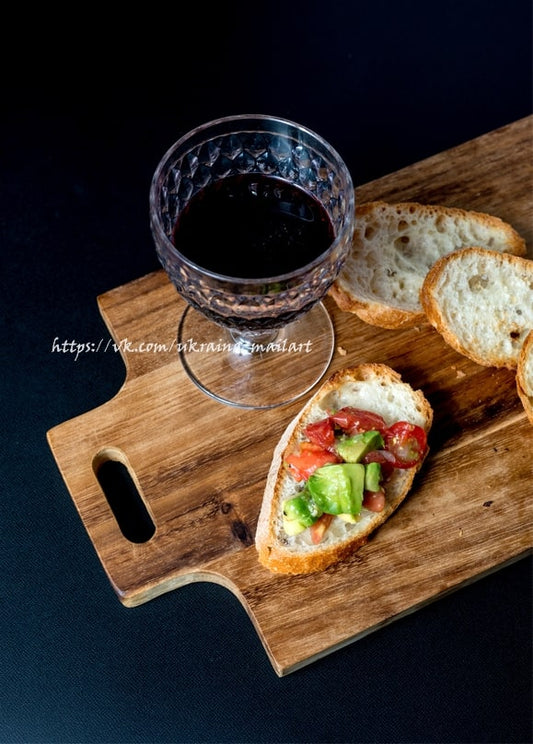 Glas Rotwein neben einer Tomaten-Avocado-Bruschetta auf einem Holzbrett