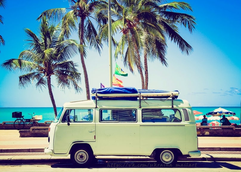 Pastellgrüner VW-Bus mit Surfbrettern unter Palmen am Strand