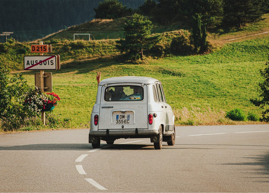 Retro-Auto fährt eine Bergstraße hinunter, eine Hand winkt aus dem Fenster