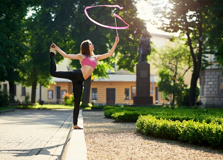 Rhythmusgymnastin balanciert mit rosa Band in einem sonnigen Park
