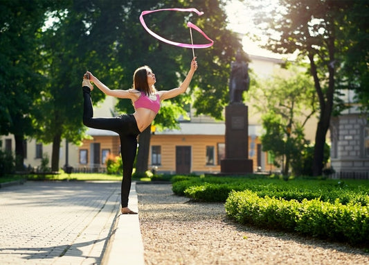 Rhythmusgymnastin balanciert mit rosa Band in einem sonnigen Park