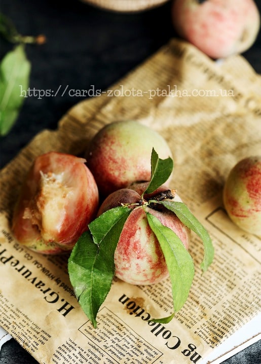 Ripe peaches with green leaves on a sheet of old newspaper, one peach bitten into