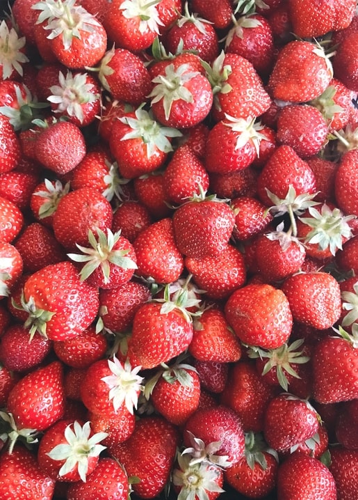 Nahaufnahme reifer roter Erdbeeren mit grünen Blattkronen, die den Rahmen füllen.