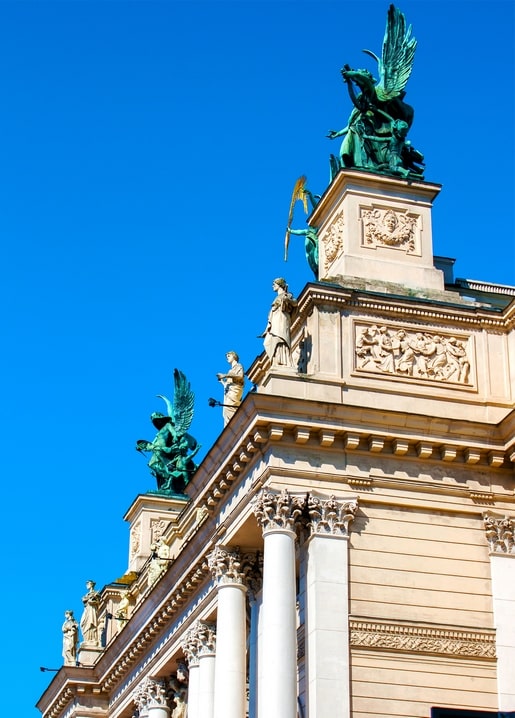 Weathered green statues atop a Lviv building against blue sky