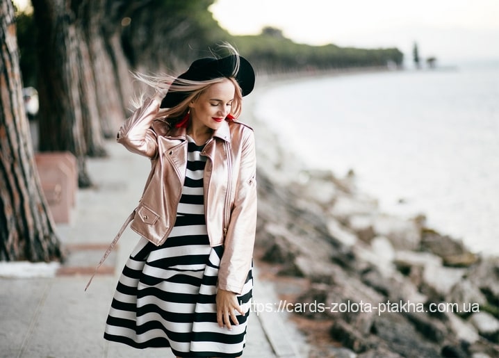 Frau in roségoldener Jacke geht eine Strandpromenade entlang