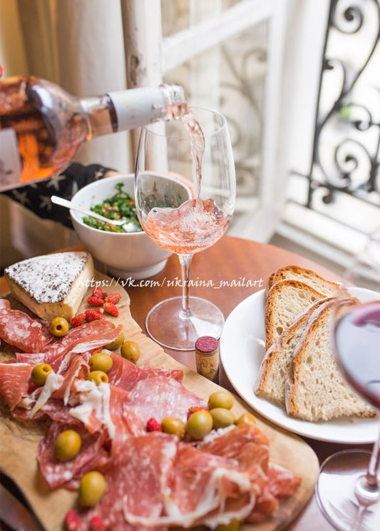 Roséwein wird ins Glas gegossen, daneben ein Prosciutto-Käse-Brett auf einem Balkontisch