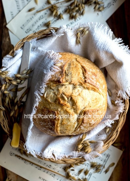 Knuspriger runder Brotlaib im Weidenkorb mit Leinentuch, Haferähren und altem Notenpapier