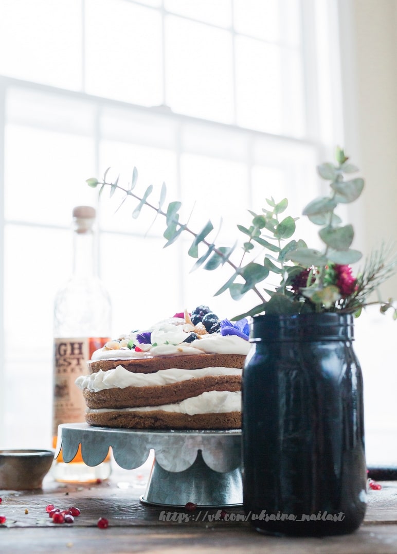 Rustic naked cake with berries and edible flowers beside a window and eucalyptus jar