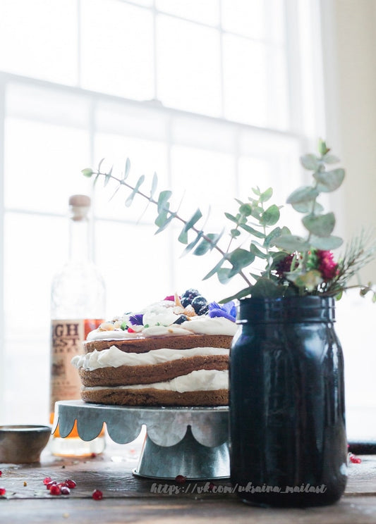 Rustikale Naked Cake mit Beeren und Blüten am Fenster neben Eukalyptus im Glas