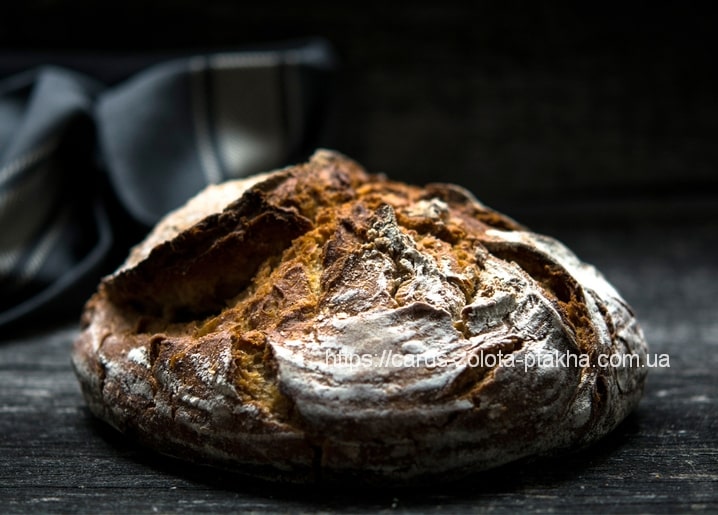 Runder Sauerteiglaib mit eingeschnittener Kruste auf dunklem Holztisch