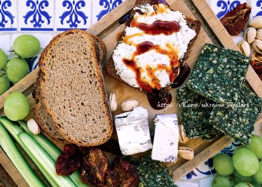 Overhead flat lay of rye toast with herbed cream cheese, balsamic drizzle, crackers, and grapes