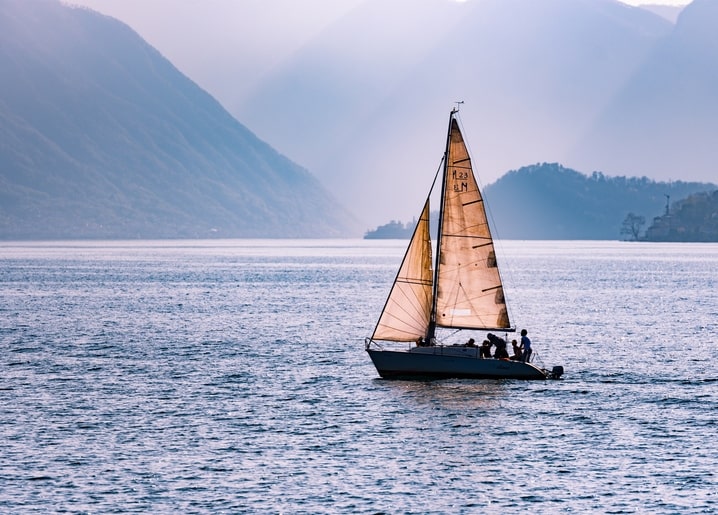 Segelboot mit goldenen Segeln auf ruhigem Bergsee bei Dämmerung