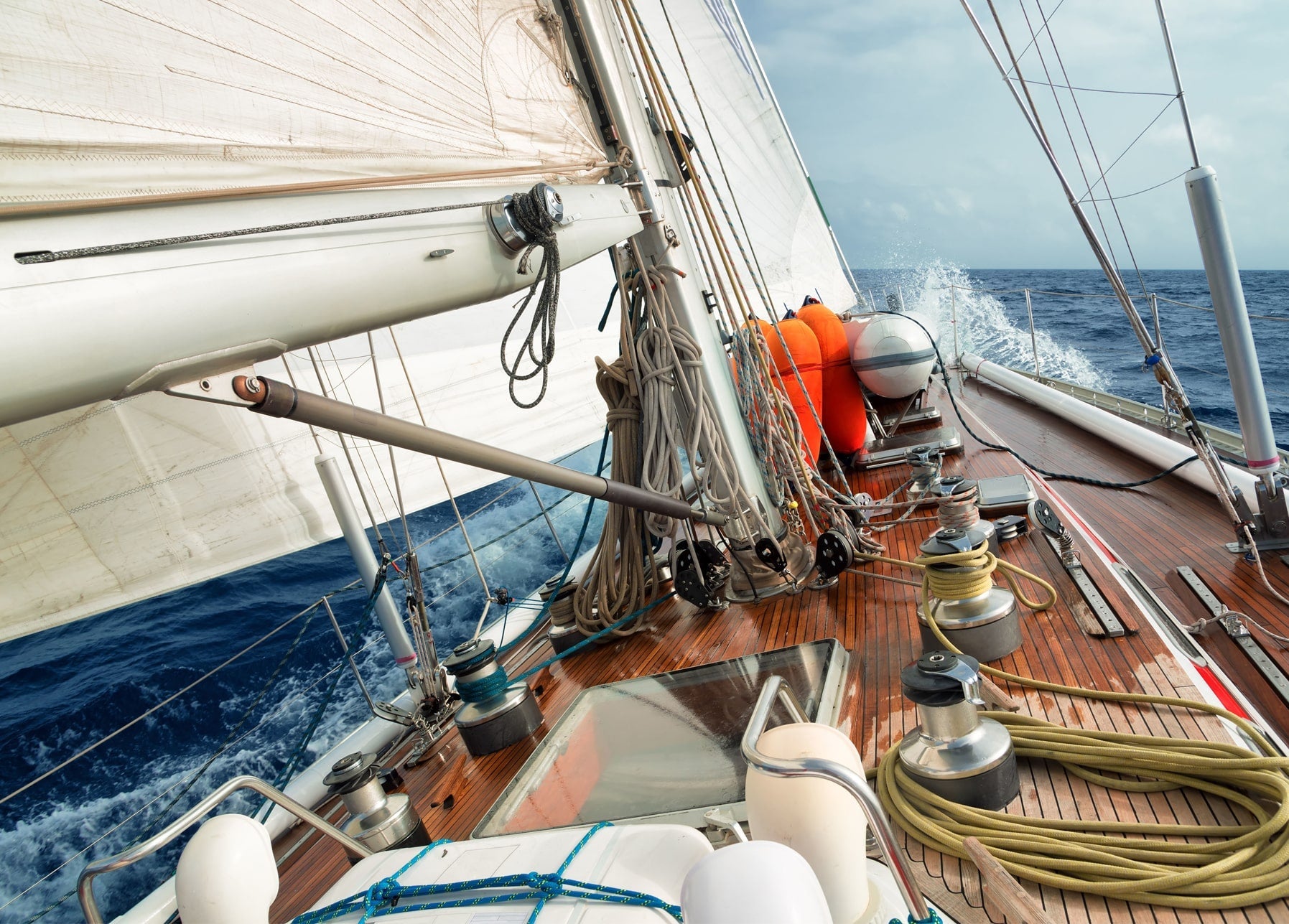 Nahaufnahme des Decks einer Segelyacht mit Tauen, Winschen und Gischt