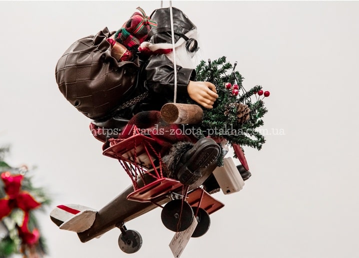 Weihnachtsmann-Figur fliegt auf einem roten Vintage-Doppeldecker mit Tannenzweig und Geschenken