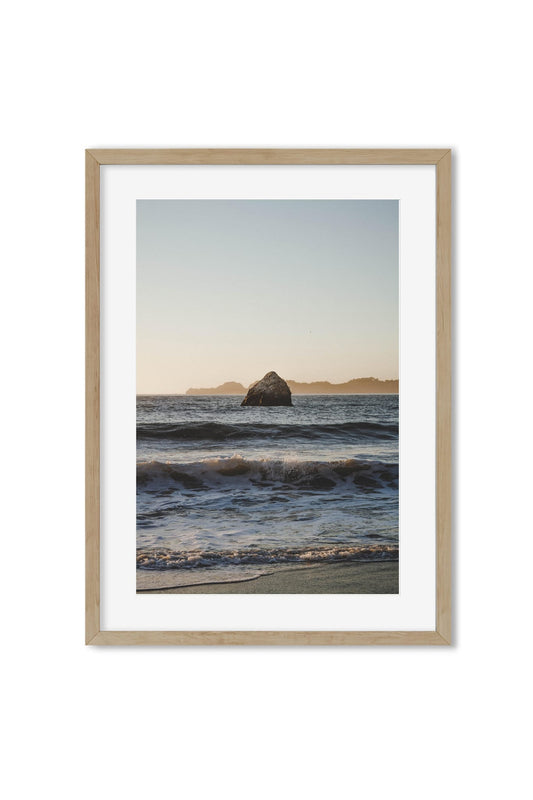 Framed poster of a sea stack rock in ocean waves at golden-hour sunset
