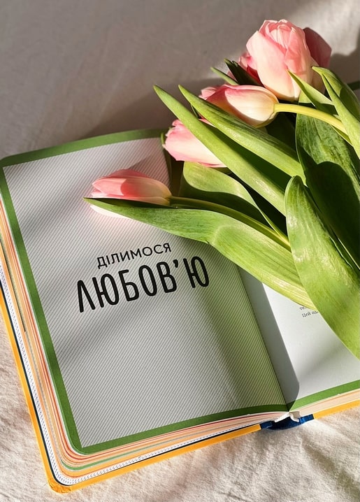 Aufgeschlagenes Buch mit der Aufschrift „Wir teilen Liebe“ unter einem Strauß rosa Tulpen