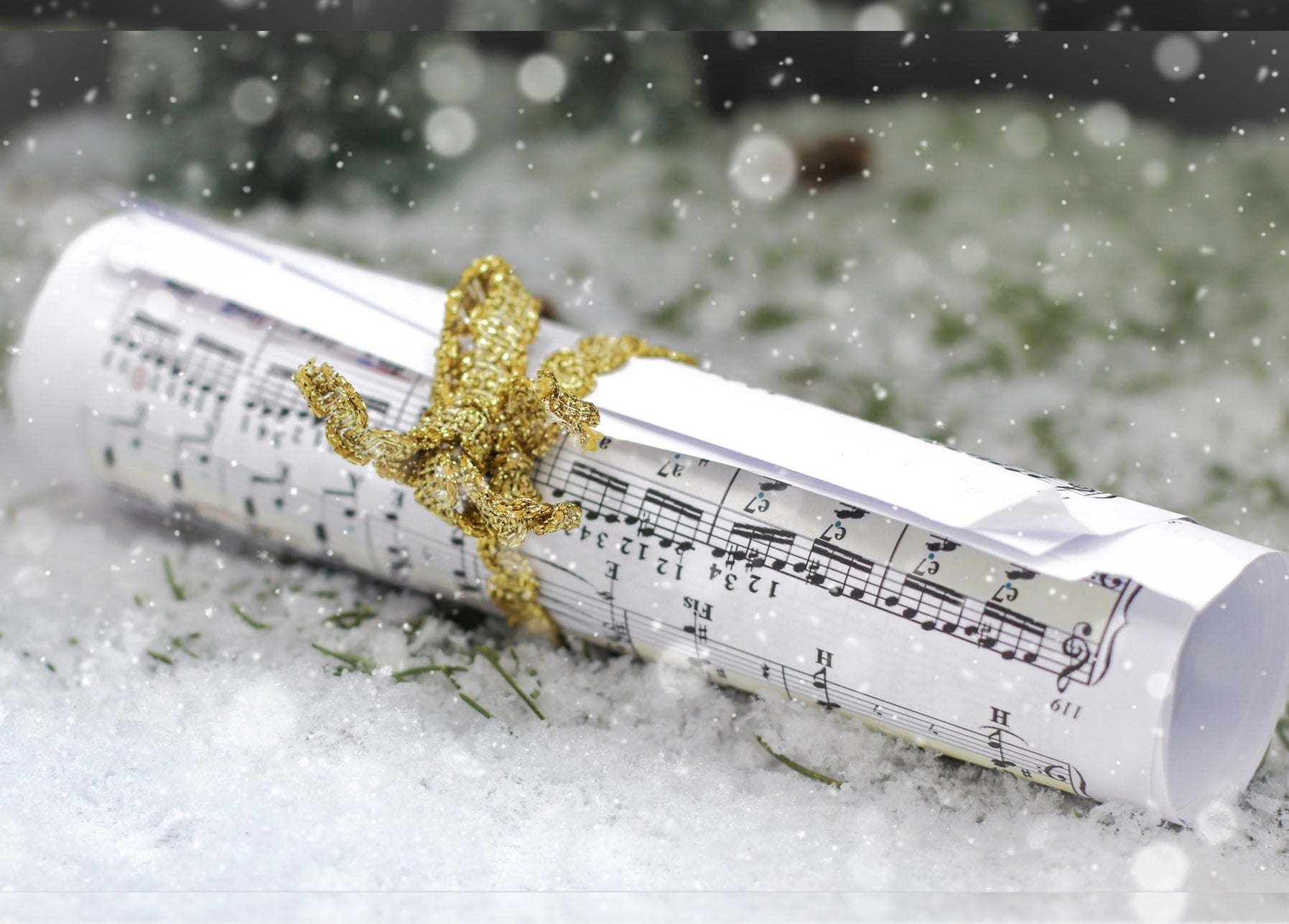 Notenblatt mit goldener Schleife liegt im Schnee mit Schneeflocken