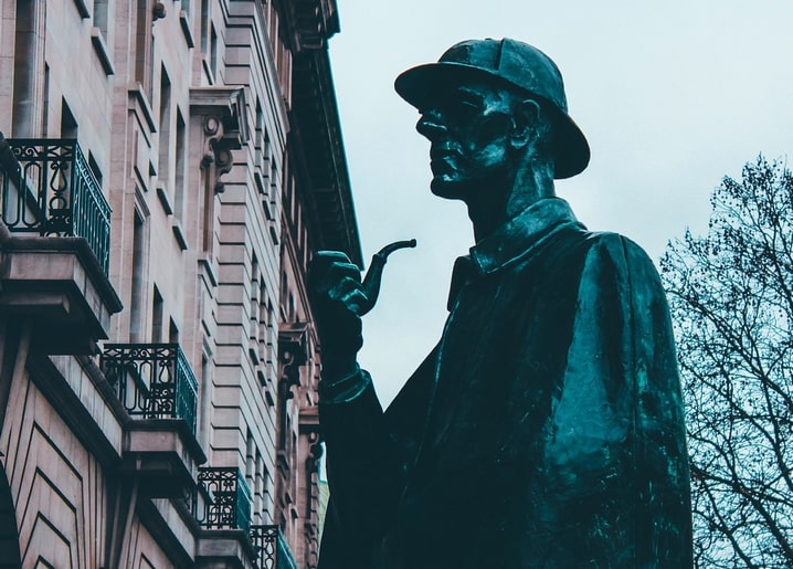 Bronze statue of Sherlock Holmes holding a pipe against townhouse balconies