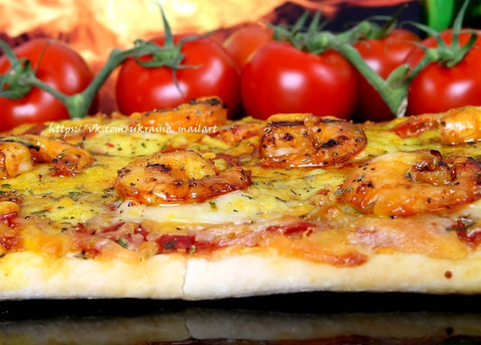 Close-up of a shrimp pizza with melted cheese next to a cluster of vine tomatoes