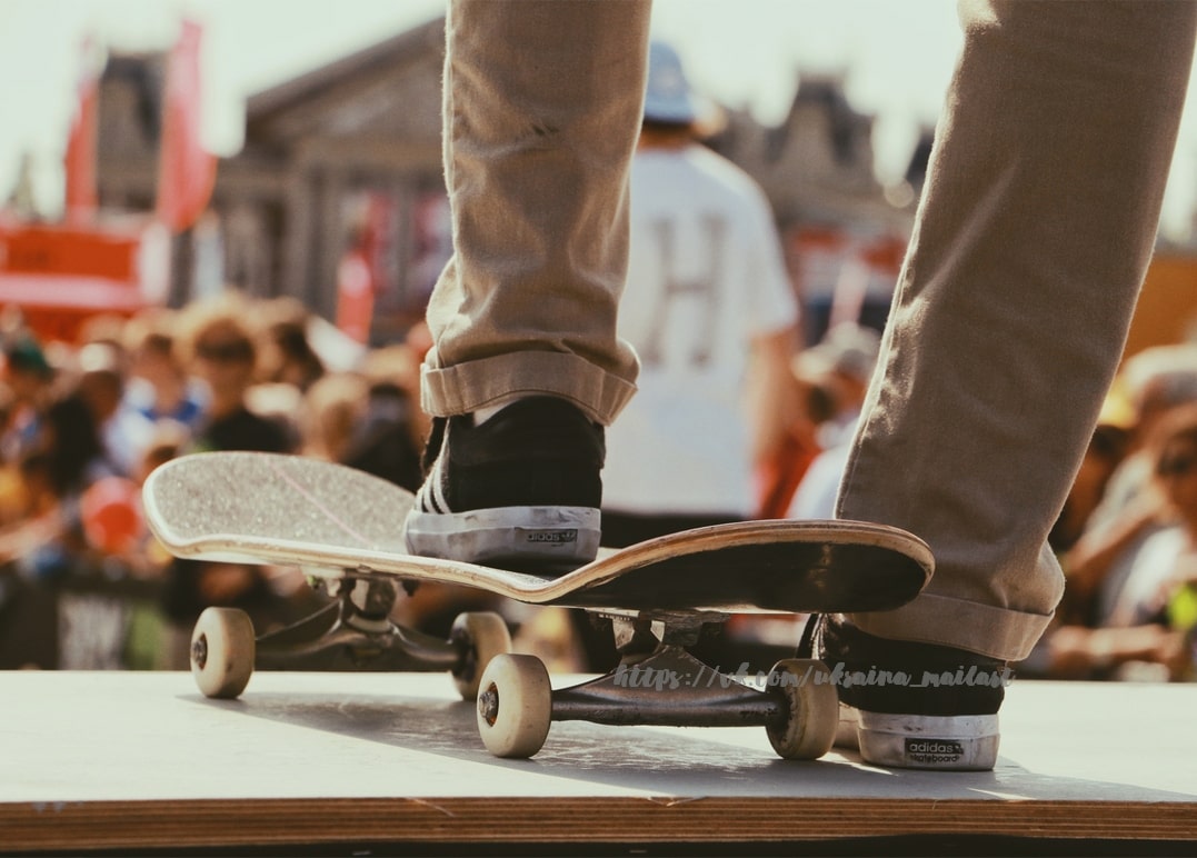 Füße eines Skateboarders balancieren auf dem Board, im Hintergrund eine Menschenmenge